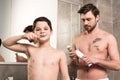 Boy brushing teeth and father holding shaving foam and brush in bathroom Royalty Free Stock Photo