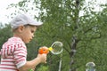 The boy in the cap lets soap bubbles in the summer against the background of green birches Royalty Free Stock Photo