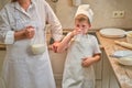 A boy in chef clothes drinks milk from a glass while cooking an apple pie in the kitchen Royalty Free Stock Photo
