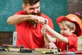 Boy, child busy in protective helmet learning to use screwdriver with dad. Father, parent with beard teaching little son