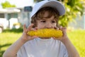 Boy child eating yellow corn with bare chest and funny face, green nature background. Autumn lifestyle. Homegrown