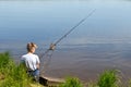 Boy child fisherman sits on shore and looks at float. Fishing with children Royalty Free Stock Photo