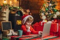 Boy child with laptop near christmas tree. Smiling little boy in Santa helper hat over xmas tree at home background Royalty Free Stock Photo