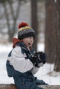 Boy child makes funny faces sitting on a log in snowy park with thermal mug. Picnic in winter