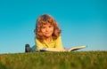 Boy child reading book, lying down on green grass. Royalty Free Stock Photo