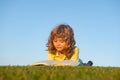 Boy child reading book, lying down on green grass. Kids adventure, freedom and carefree children.