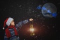 Boy in Christmas hat with lantern in hand, points the way Santa Claus flying on his sleigh with the moon Royalty Free Stock Photo