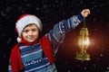 Boy in Christmas hat with lantern in hand, points the way Santa Claus flying on his sleigh with the moon Royalty Free Stock Photo