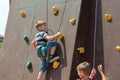 A boy in climbing equipment conquers the top of an artificial tower for climbers in a sports extreme recreation park