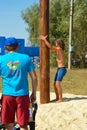 Boy climbing up on wooden slippery column to take the red woman boots