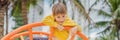The boy climbs on the playground against the background of palm trees BANNER, LONG FORMAT Royalty Free Stock Photo