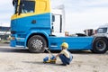 boy in construction helmet plays with toy car while sitting on construction site in front of dump truck cabin Royalty Free Stock Photo
