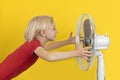 Boy cools off with ventilator. Child holds the fan on yellow background. Hot weather