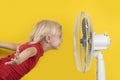 Boy cools off with ventilator. Portrait on yellow background. Summer heat Royalty Free Stock Photo