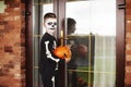 A boy in a costume and festive makeup with a pumpkin lantern Jack, knocking on the door for sweets on a halloween party