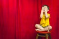 Boy Covering Eyes Sitting on Stool in Front of Red Curtain