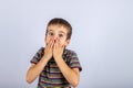 boy covers his mouth with two hands from fright on a blue background