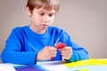 Child cutting colored paper with scissors at the table Royalty Free Stock Photo