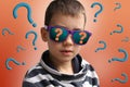 Boy in dark sunglasses, the reflection of which depicts a question mark, in a striped sweater, surrounded by many question marks,