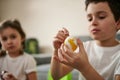 Boy decorating an Easter egg with yellow gouache. Closeup of hands on the background of blurry children