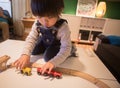 A boy in denim overalls is playing with a wooden train toy attentively Royalty Free Stock Photo