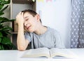 The boy doesn`t want to read the book. A boy in a gray T-shirt sits at a white table at the open book and holds his hand behind