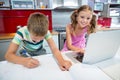 Boy doing his homework while girl using laptop in kitchen Royalty Free Stock Photo