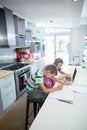 Boy doing his homework while girl using laptop in kitchen Royalty Free Stock Photo