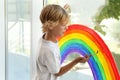 Boy drawing rainbow on window. Stay at home concept