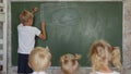 The boy draws on the board in front of his sisters and brothers.