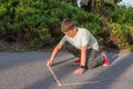 The boy draws on the pavement with colored chalk in the park. Drawing