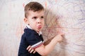 The boy draws on the wall and grimaces. The child is engaged in creativity at home Royalty Free Stock Photo