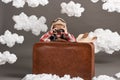 Boy dressed as an airplane pilot sit between the clouds with old suitcase and playing with handmade plane