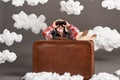 Boy dressed as an airplane pilot sit between the clouds with old suitcase and playing with handmade plane Royalty Free Stock Photo