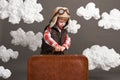 Boy dressed as an airplane pilot stand between the clouds with old suitcase and playing with handmade plane Royalty Free Stock Photo