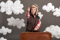 Boy dressed as an airplane pilot stand between the clouds with old suitcase and playing with handmade plane Royalty Free Stock Photo