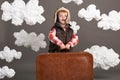 Boy dressed as an airplane pilot stand between the clouds with old suitcase and playing with handmade plane Royalty Free Stock Photo