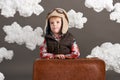 Boy dressed as an airplane pilot stand between the clouds with old suitcase and playing with handmade plane Royalty Free Stock Photo