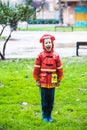 Boy dressed as a fireman with red raincoat splashes on the grass of a park a rainy day