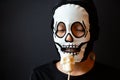 Boy dressed as a skeleton holding a skull lollipop in his hand on the black background