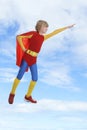 Boy dressed as superhero flying against cloudy sky