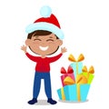 The boy is dressed in a Santa Claus hat and stands right next to the gifts. The child is happy and smiling. Royalty Free Stock Photo