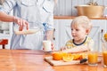 The boy drinks milk from a glass. Mother and son are smiling while having a breakfast in kitchen. Mom is pouring milk Royalty Free Stock Photo