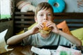 Boy eating a big burger with a cutlet. Hamburger in the hands of a child. Delicious and satisfying chicken cutlet burger.