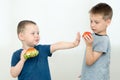 The boy eats a hamburger and refuses fruit offered by a friend. 2 boys on a light background. The concept is to lead a healthy