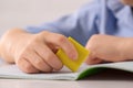 Boy erasing mistake in his notebook at white desk, closeup