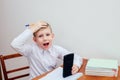 A boy of European appearance in a white shirt sits at a table and holds his head Royalty Free Stock Photo