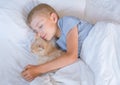 the boy falls asleep and hugs his ginger cat, who sleeps with him under the covers. children and pets. the cat sleeps Royalty Free Stock Photo