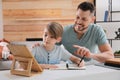 Boy with father doing homework using tablet at table in room Royalty Free Stock Photo