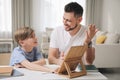 Boy with father doing homework using tablet at table in room